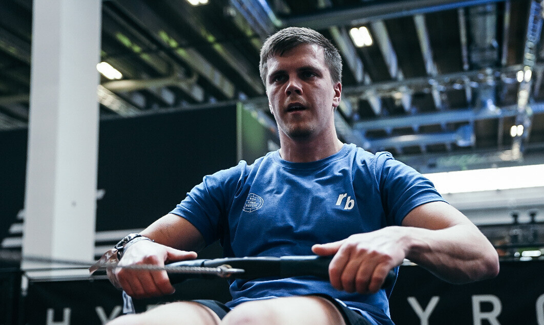 Atlet der rower ved HYROX Copenhagen med HYROX-skiltet i baggrunden